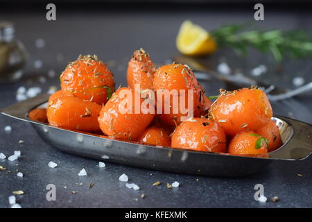 Glassato al miele carotine con sale marino e timo in un recipiente di metallo posto su un grigio Sfondo astratto. Il mangiare sano concetto. il digiuno cibo. pasto sano Foto Stock