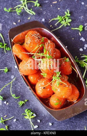 Glassato al miele carotine con sale marino e timo in un recipiente di metallo posto su un grigio Sfondo astratto. Il mangiare sano concetto. il digiuno cibo. pasto sano Foto Stock