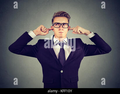 Orinato uomo collegando le orecchie con le dita non vuole ascoltare isolato sul muro grigio sfondo Foto Stock