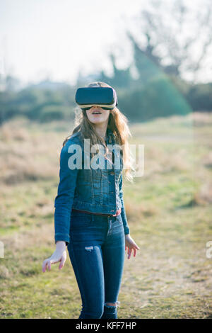 Ragazza vestita in denim nella luce del sole che indossa la realtà virtuale auricolare all'aperto Foto Stock