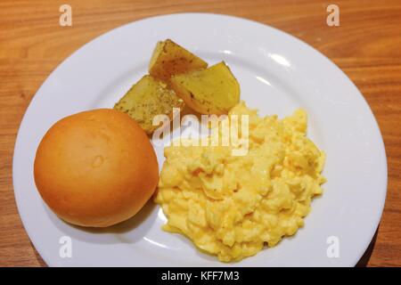 La cucina e il cibo, piastra di deliziose uova strapazzate con pane tondo e patate alla griglia su un tavolo di legno. Foto Stock