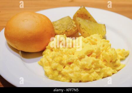 La cucina e il cibo, piastra di deliziose uova strapazzate con pane tondo e patate alla griglia su un tavolo di legno. Foto Stock