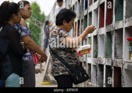 Carreta Cemetery, Cebu City, Filippine. 28 ottobre 2017. Una famiglia stand prima di una tomba di una persona amata come una donna recita una preghiera mentre tiene Beads Rosary. Tutti i Santi giorno & tutte le anime giorno che cade il 31 ottobre e 1 novembre rispettivamente vedrà milioni di filippini che frequentano cimiteri in tutto il paese per ricordare i parenti defunti & cari. Credit: Imagegallery2/Alamy Live News Foto Stock