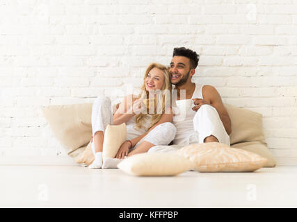 Coppia giovane seduto sul pavimento di cuscini, sorriso ispanico l uomo e la donna amanti in camera da letto Foto Stock