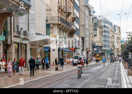Unidentified pedoni e un uomo in sella a una moto in Rue de la Croix-d'o sotto un cielo nuvoloso. Ginevra, Svizzera. Foto Stock