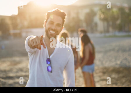 Ritratto di uomo felice sulla spiaggia puntando alla fotocamera Foto Stock