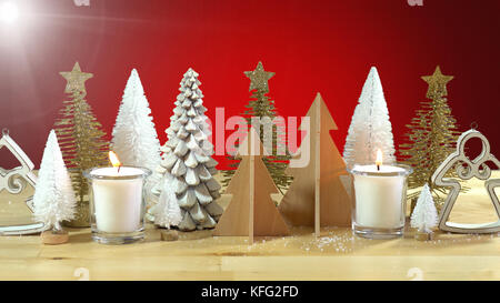 Centrotavola di natale o mantel decorazione di righe della miniatura di alberi di Natale con candele accese contro uno sfondo di colore rosso, con la luce flare. Foto Stock