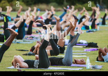 Atlanta, GA, Stati Uniti d'America - 2 luglio 2, 2017: decine di persone fanno un yoga pongono giacenti sulle loro spalle come essi prendono parte in un gruppo libero yoga classe. Foto Stock