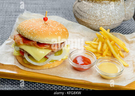 Formaggio hamburger con bakon guarnita con salse e patate fritte Foto Stock