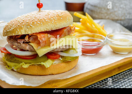 Formaggio hamburger con bakon guarnita con salse e patate fritte Foto Stock