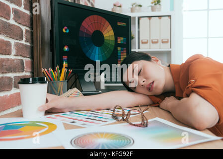 Bella giovane azienda di graphic design femminile di lavoro dipendente tempo lungo e disteso sulla scrivania in ufficio di riposo del sonno. Foto Stock