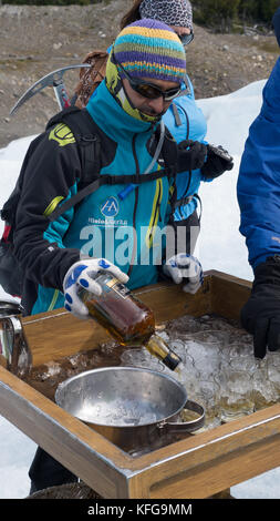 Guida turistica locale analizzato piccoli bicchieri di whiskey su ghiacciaio al fine di escursionismo su ghiacciaio. Bottiglia in mano con piccozza strapped sul retro. Foto Stock