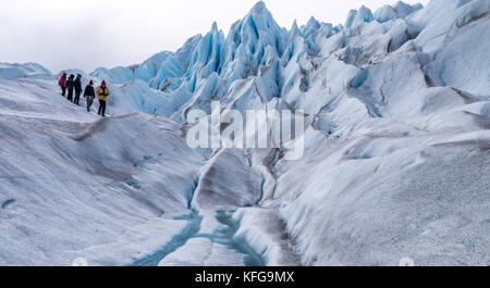 Guide leader di un gruppo di colorfully vestito i turisti in una breve escursione sul ghiacciaio con il cielo blu, il paesaggio glaciale, correnti e vette glaciali Foto Stock