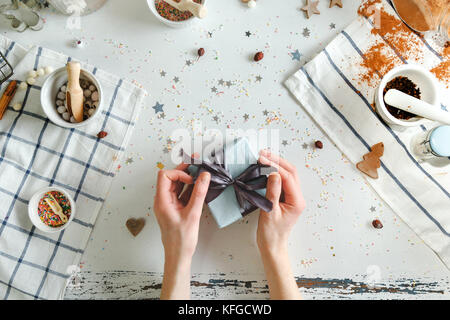 Ragazza confezioni regalo di Natale scatola con un nastro di colore blu su un fatti a mano nella tabella. Foto Stock