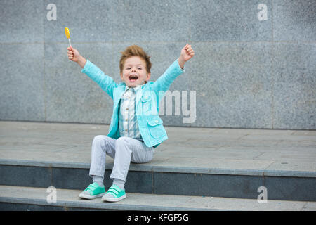 Moda capretto con lollipop vicino al muro grigio Foto Stock