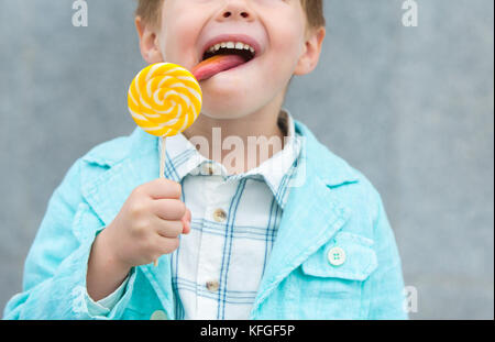 Moda capretto con lollipop vicino al muro grigio Foto Stock