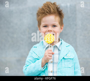 Moda capretto con lollipop vicino al muro grigio Foto Stock