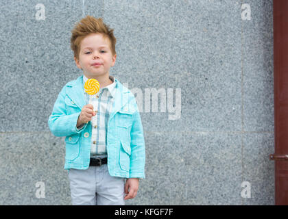 Moda capretto con lollipop vicino al muro grigio Foto Stock