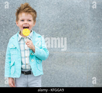 Moda capretto con lollipop vicino al muro grigio Foto Stock