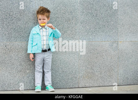 Moda capretto con lollipop vicino al muro grigio Foto Stock