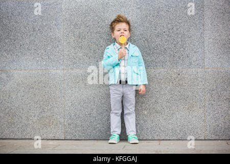 Moda capretto con lollipop vicino al muro grigio Foto Stock