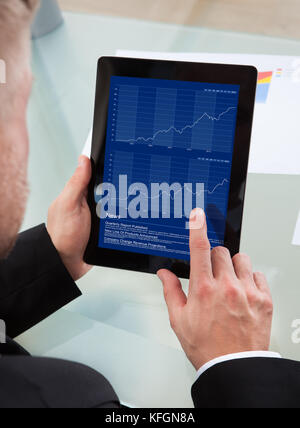 Imprenditore la navigazione sul suo tablet pc utilizzando il suo dito sul touchscreen come egli studi un report online oltre la spalla vista dello schermo Foto Stock