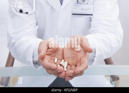 Medico o infermiere in un bianco camice da laboratorio con le compresse di contenimento nelle sue mani a tazza offrendo loro al visualizzatore vista ravvicinata delle sue mani Foto Stock