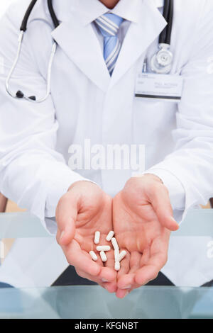 Medico o infermiere in un bianco camice da laboratorio con le compresse di contenimento nelle sue mani a tazza offrendo loro al visualizzatore vista ravvicinata delle sue mani Foto Stock