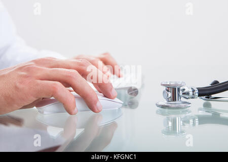 Conceptual medico e sanitario immagine con una chiusura di uno stetoscopio giacente su un banco medici con le mani del medico visibile dietro o di lavoro Foto Stock