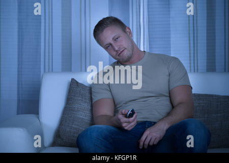 L'uomo rilassante sul divano e tenendo premuto il telecomando del TV Foto Stock