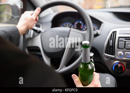 Primo piano della bottiglia di birra Man Holding durante la guida dell'auto Foto Stock