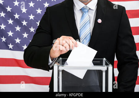 Persona nella bandiera americana anteriore che mette il ballottaggio nella scatola di vetro Foto Stock