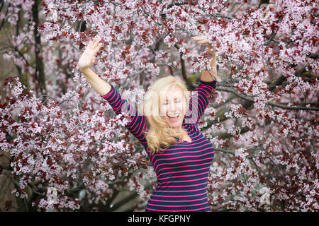 Bionda capelli lunghi donna caucasica ridere vicino a fioritura tree Foto Stock