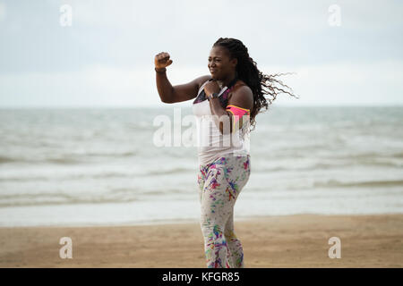 Attraente sportivo donna africana facendo esercizi di boxe sulla spiaggia sotto la pioggia Foto Stock