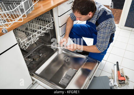 Tecnico maschile seduto vicino alla lavastoviglie scrivendo su Appunti in cucina Foto Stock