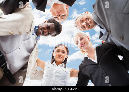 Angolo basso ritratto della società multietnica la gente di affari formando huddle contro sky Foto Stock