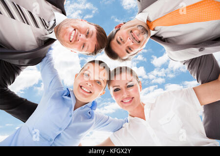 Direttamente sotto il ritratto di felice la gente di affari formando huddle contro sky Foto Stock