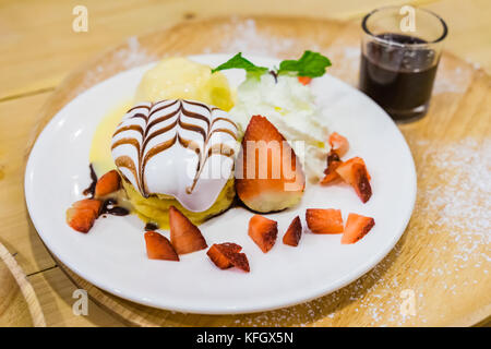 Deliziosi pancake con fragole e gelato alla vaniglia con topping di cioccolato e panna montata su sfondo di legno Foto Stock