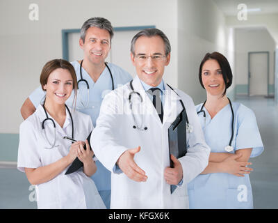 Ritratto di felice senior medico handshake offerta permanente, mentre con il team in ospedale Foto Stock