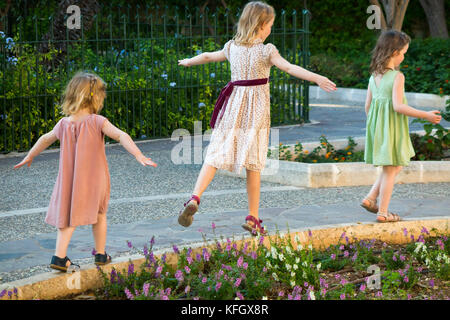 Tre giovani sorelle / ragazze / ragazzi / bambini / bambino di età compresa tra i 7, 3, & 5 anni sulla famiglia vacanze equilibrio, correre e giocare in Lower Barrakka Gardens. Malta Foto Stock