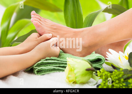 Immagine ritagliata della massaggiatrice che massaggiano il piede della donna contro le foglie della spa Foto Stock