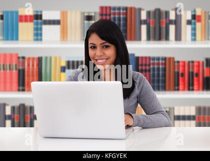 Ritratto di giovane donna felice in biblioteca utilizzando laptop Foto Stock