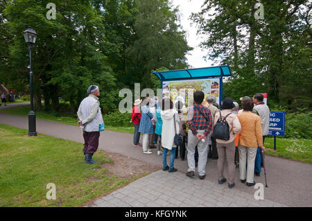 Gruppo di turisti vicino al segno di informazioni di Muckross House e giardini, Parco Nazionale di Killarney, nella contea di Kerry, Irlanda Foto Stock