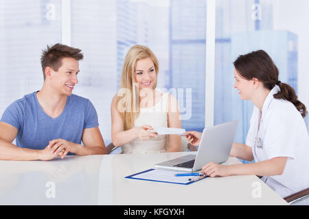 Medico donna dando carta di prescrizione alla coppia giovane alla reception in clinica Foto Stock