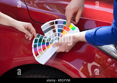 Immagine ritagliata del meccanico che mostra i campioni di colore per il cliente contro auto Foto Stock