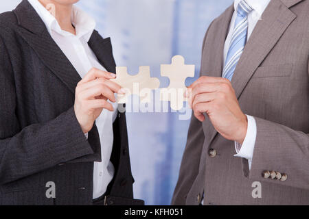 Sezione mediana di imprenditore e imprenditrice unire pezzi di puzzle in office Foto Stock