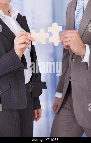 Sezione mediana di imprenditore e imprenditrice unire pezzi di puzzle in office Foto Stock