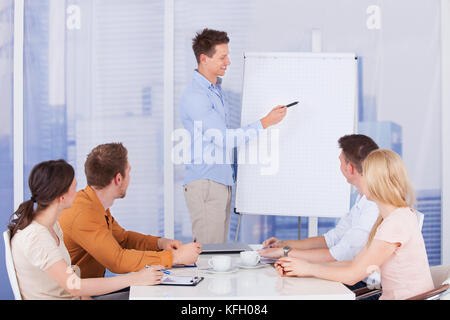 Giovane imprenditore dando la presentazione ai colleghi in ufficio Foto Stock