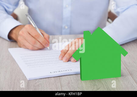 Sezione mediana di imprenditore firma un contratto con il verde casa modello alla scrivania
