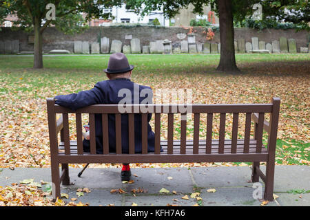 Il vecchio uomo seduto su un banco in un parco di San Giorgio chiesa trattativa con lapidi intorno al perimetro, trattare, Kent, England, Regno Unito, Europa Foto Stock